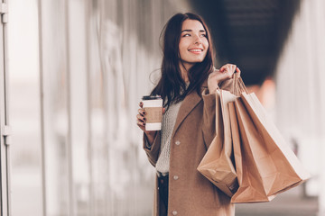 Beautiful fashionable woman with shopping bags and coffee walking near mall.