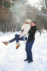 Fototapeta na wymiar Young stylish couple in love have fun while walking on the snowy winter park. Handsome young man holds his beautiful girl on the hands.