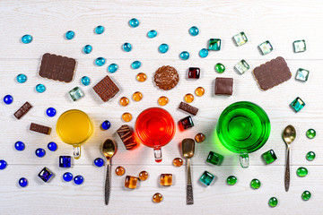 Three carbonated drinks green, yellow, red in different glass mugs with teaspoons surrounded by...