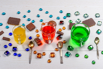 Three carbonated drinks green, yellow, red in different glass mugs with teaspoons surrounded by...