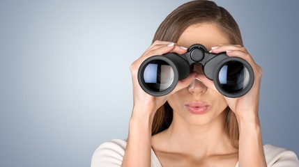 Girl looking into binoculars on light background