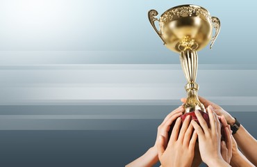 Close-up human hand holding golden Trophy on blurred blue background