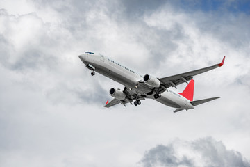 Plane with two turbofan engines, landing gear and red winglets on cloud background