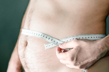 Obese nude man with white measuring tape holding in hand