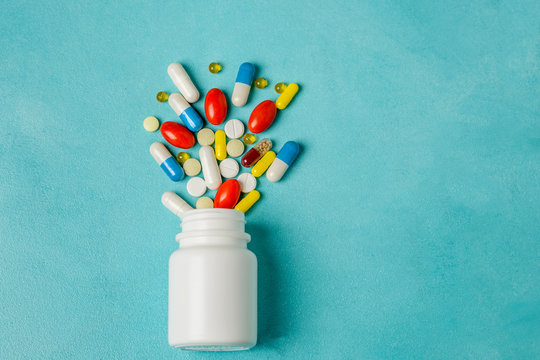 Pills in white pill bottle on light blue background, a lot of colorful tablets with copy space