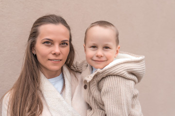 happy and young family, a woman mom holds in her arms a little boy son, happy smiling posing, warm autumn clothes. Emotions of comfort, joy of the holiday and care of love.
