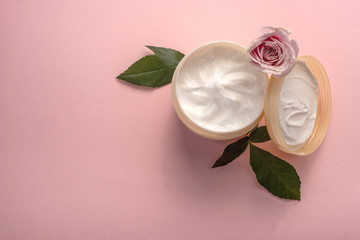 The jar of skin care or body care cream with lid and rose flower with leaves on pink background, copy space