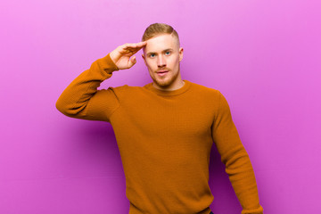 young blonde man wearing a jumper greeting the camera with a military salute in an act of honor and...