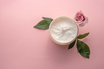 The jar of skin care or body care cream with rose flower with leaves on pink background, top view