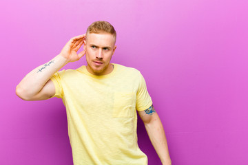 young blonde man wearing yellow t shirt looking serious and curious, listening, trying to hear a...