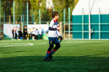 Obraz premium Boys in white and blue sportswear plays football on field, dribbles ball. Young soccer players with ball on green grass. Training, football, active lifestyle for kids concept 