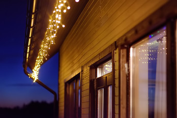 Cozy scene of string lights hanging under the roof at evening time. Christmas party. Outdoor...