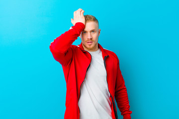 young blonde man wearing sports clothes raising palm to forehead thinking oops, after making a...