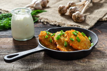 potato pancakes with meat and sour cream lie in a pan seasoned with greens, onions and dill. frying pan with pancakes stands on old wooden background