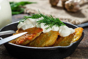 potato pancakes with meat and sour cream lie in a pan seasoned with greens, onions and dill. frying pan with pancakes stands on old wooden background