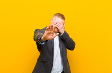 young blond businessman covering face with hand and putting other hand up front to stop camera, refusing photos or pictures - Powered by Adobe