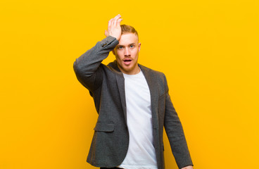 young blond businessman raising palm to forehead thinking oops, after making a stupid mistake or...