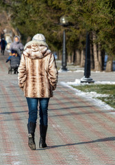 A girl in a fur coat walks along the street, autumn cold day.