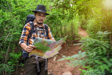 man traveler with backpack and map searching directions in the forest