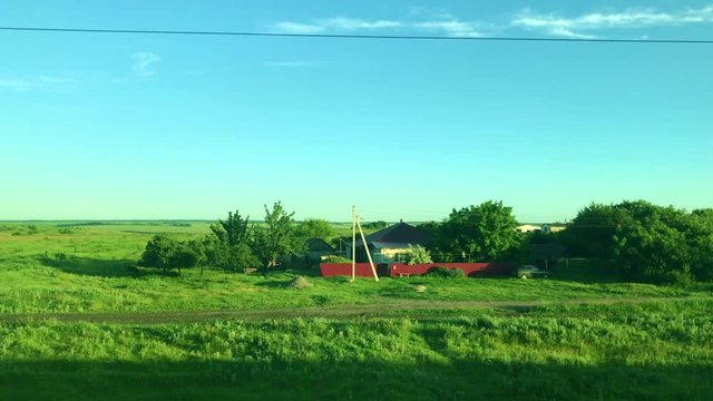 View, scenery from the window of a moving train with green landscape, fields, hills and villages