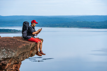 hiker man sitting and using smartphone on edge of cliff, on a top of the rock mountain - Powered by Adobe