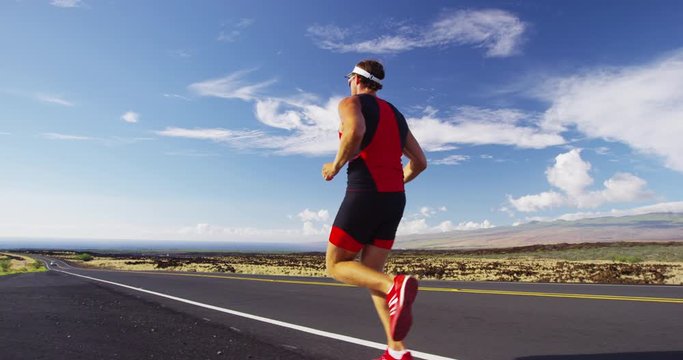 Runner man running in triathlon suit training for Iron man on Hawaii. Fit male triathlete exercising on road. REAL TIME RED Cinema Camera.