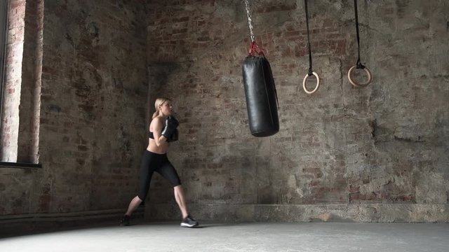 Taekwondo Professional Athlete Woman Kicks The Punches Bag In Gym. Athletic Kickboxing Woman. Girl Punches And Kicks The Punches Bag In Gym. Smiling girl