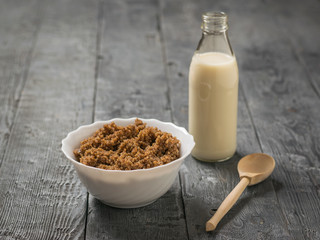Quinoa porridge with cocoa and a bottle of almond milk on a wooden table.