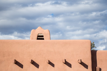 A adobe building on a sunny day with clouds in the background.