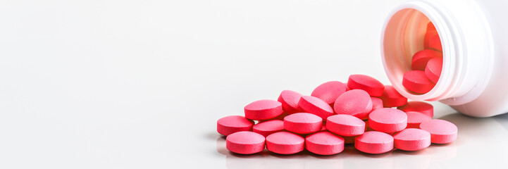 Red pills are scattered from a jar on a white background.