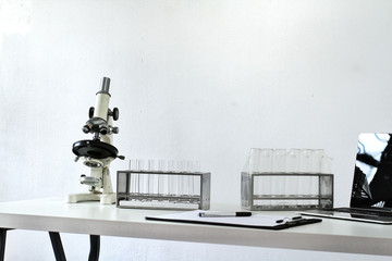 Microscope and group of test tubes on rack, white table in gray wall background, copy space for text. Science lab technology education research project concept.