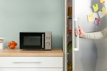 Woman opening modern fridge in kitchen