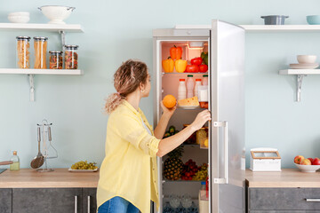 Woman choosing food in modern fridge at home