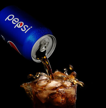 POLTAVA, UKRAINE - MARCH 22, 2018: Splash pepsi into a glass on a black background. Pepsi is a carbonated soft drink produced PepsiCo. Created in 1893