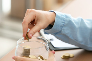 Fototapeta na wymiar Woman putting coins into jar on table. Money savings concept