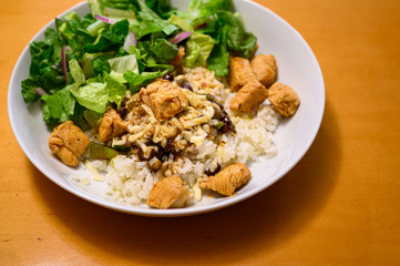 Close up of beans and rice, frijoles, with chicken, in a white bowl, with salad greens
