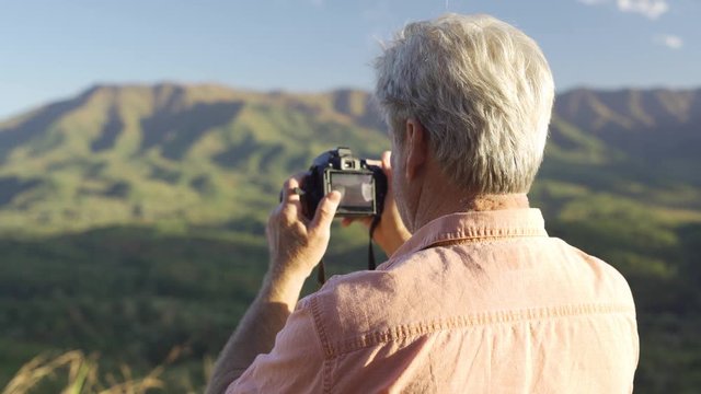 Older man , senior citizen on vacation trying to use dslr camera to take picture but having trouble