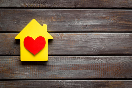 Happy life and home concept. House cutout and heart icon on dark wooden background top view copy space