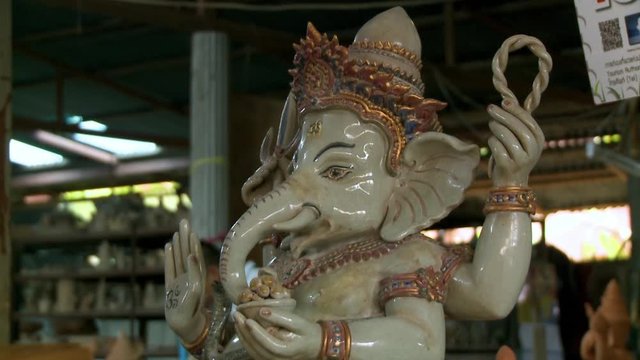 A daylight closeup shot of a glazed ceramic interpretation of the Hindu God, Ganesha, featured amongst other artifacts inside a pottery factory.
