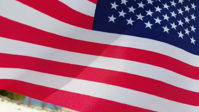 Close up of American flag with white and red stripes, white stars on blue field, waving on light breeze of exotic beach, concept design