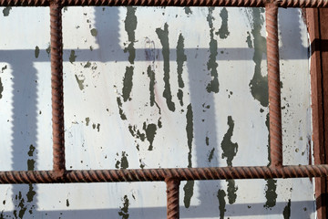 Old window painted by white paint behind a rusty brown bars on a sunny day. Abstract background