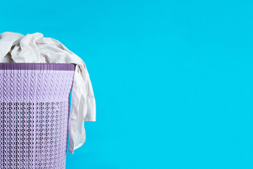 over flowing purple laundry basket with white shirt dangling on the side isolated on a light blue background 