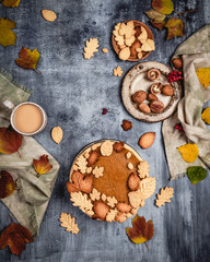 traditional pumpkin pie decorated with leaves shaped cookies on shabby blue background with coffee and textile