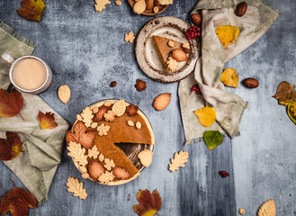 Obraz na płótnie Canvas traditional pumpkin pie decorated with leaves shaped cookies on shabby blue background with coffee and textile