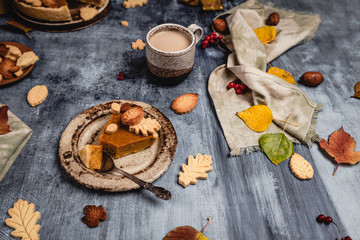 traditional pumpkin pie decorated with leaves shaped cookies on shabby blue background with coffee and textile