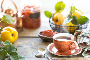 Cup of tea with homemade quince jam on an old wooden background. Fresh fruits and quince leaves on the background. Horizontal photo. rustic
