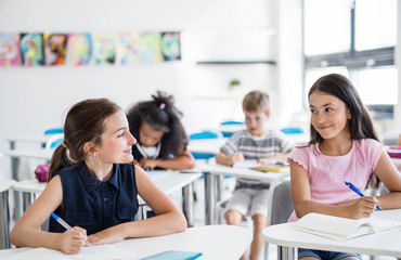 School children sitting at the desk in classroom on the lesson, talking.