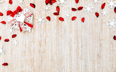 Flat lay shabby Christmas copy space with white wooden snowflakes, red petals and a white wooden decorative heart in the upper left corner on light wooden background