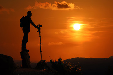 Photographer taking pictures on the mountain over sunset background