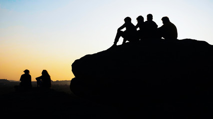 Silhouette of group people sits and admiring the sunset on top of mountain.